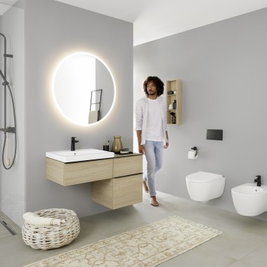 Homme entrant dans une salle de bains équipée d’un lavabo, d’un WC, d’un bidet et de meubles de la collection Geberit iCon.